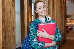 Smiling high school girl with headphones and backpack holding folder