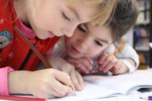 Two little girls writing in school workbook 